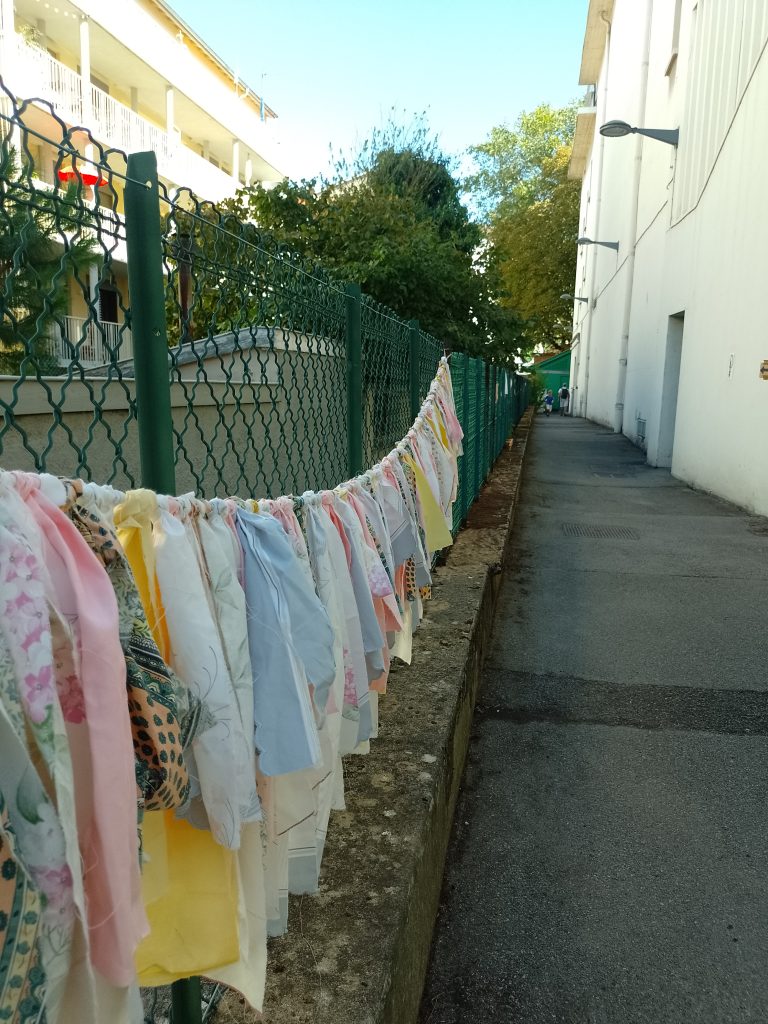 Passage entre le théâtre et le clos bouliste : décoration du grillage avec des chutes de tissus colorés en guirlande