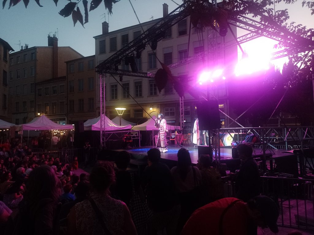 Place du théâtre, show drag, soirée : artiste drag du collectif des merveilles qui chante sur scène avec de la lumière rose
